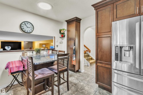 Kitchen with a granite-top island, extensive wood cabinetry, and a built-in stainless steel refrigerator - 76 Gariepy Crescent Nw, Edmonton, AB 