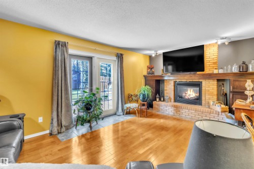 Hardwood flooring, brick-surround fireplace with hearth, built-in shelving, track lighting, and double glass doors - 76 Gariepy Crescent Nw, Edmonton, AB 