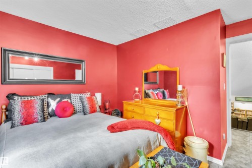 Textured ceiling with white trim, solid red wall finish, and a wood-finish dresser with an attached mirror - 76 Gariepy Crescent Nw, Edmonton, AB 