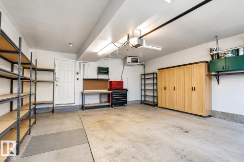 Expansive garage featuring a concrete floor, built-in wooden cabinetry, wall-mounted shelving, overhead lighting, and a white entry door - 76 Gariepy Crescent Nw, Edmonton, AB 