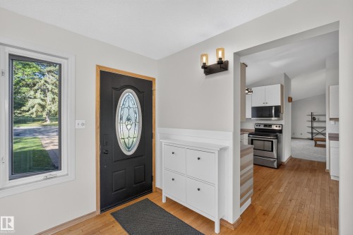 Entryway featuring a decorative glass-insert door, wood-finish flooring, and a wall-mounted light fixture - 23 Clearwater, Devon, AB 