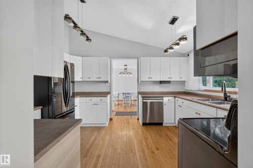 Kitchen featuring wood-finish flooring, white cabinetry, dark countertops, and stainless steel appliances - 23 Clearwater, Devon, AB 
