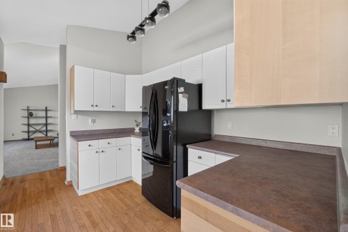 Kitchen featuring wood-finish flooring, white cabinetry, dark countertops, and a black refrigerator - 23 Clearwater, Devon, AB 