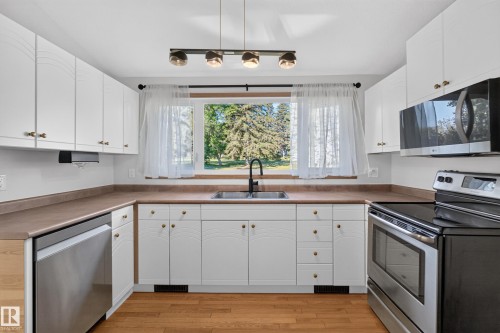 Kitchen featuring white cabinetry, wood-finish flooring, stainless steel appliances, and a window with exterior views - 23 Clearwater, Devon, AB 