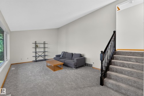 Spacious living area featuring high vaulted ceilings, large windows, plush gray carpeting, and a dark wood-finish staircase with balusters - 23 Clearwater, Devon, AB 