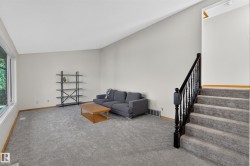 Spacious living area featuring high vaulted ceilings, large windows, plush gray carpeting, and a dark wood-finish staircase with balusters - 