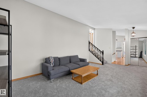Light gray carpeting throughout, featuring a staircase with black spindle railing, wood-finish baseboards, and a contemporary ceiling fixture - 23 Clearwater, Devon, AB 