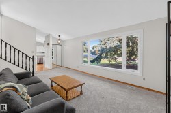 Expansive main-level room featuring a large picture window, light gray carpeting, and a staircase with a black metal railing - 