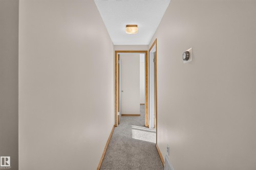 Hallway featuring neutral-toned walls, gray carpeting, and wooden door frames - 23 Clearwater, Devon, AB 