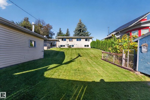 Expansive sloped lawn with mature evergreen trees, established shrubbery, and a wooden fence - 23 Clearwater, Devon, AB 