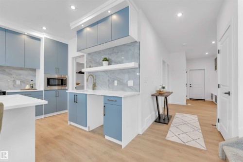 Modern kitchen featuring light blue cabinetry, white countertops, recessed lighting, wood-finish flooring, and a stainless steel built-in microwave - 2 Tenuto Link, Spruce Grove, AB 