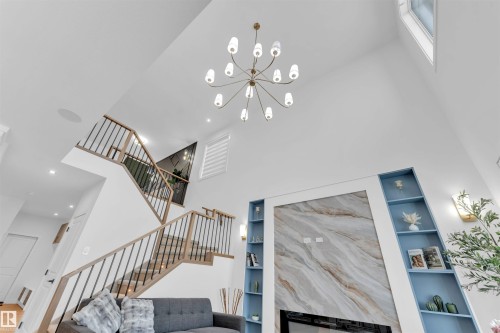 Vaulted ceilings with a multi-arm chandelier, built-in shelving, fireplace with a stone-finish surround, and a two-story staircase with metal balusters - 2 Tenuto Link, Spruce Grove, AB 