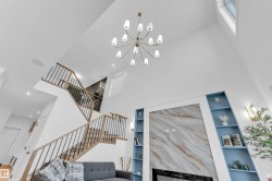 Vaulted ceilings with a multi-arm chandelier, built-in shelving, fireplace with a stone-finish surround, and a two-story staircase with metal balusters - 