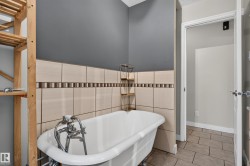 Clawfoot soaking tub with floor-mounted fixtures, ceramic wall tile with accent trim, and neutral floor tile - 