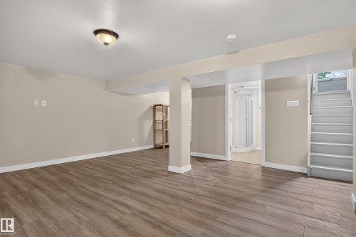 Spacious room featuring wood-finish flooring, neutral-toned walls, overhead lighting, and an accessible staircase - 11549 88 Street Nw, Edmonton, AB 
