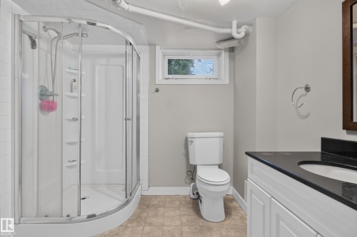 Curved glass shower enclosure with white tile surround, vanity with dark countertop, and built-in toilet - 11549 88 Street Nw, Edmonton, AB 
