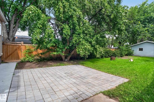Private backyard featuring a paver patio, lush green lawn, mature trees, and a wood fence - 11549 88 Street Nw, Edmonton, AB 