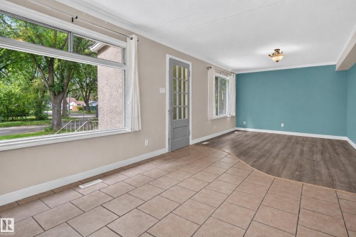 Tiled flooring transitioning to wood-finish flooring, large window with white trim, French door with glass panels, and a ceiling-mounted light fixture - 11549 88 Street Nw, Edmonton, AB 