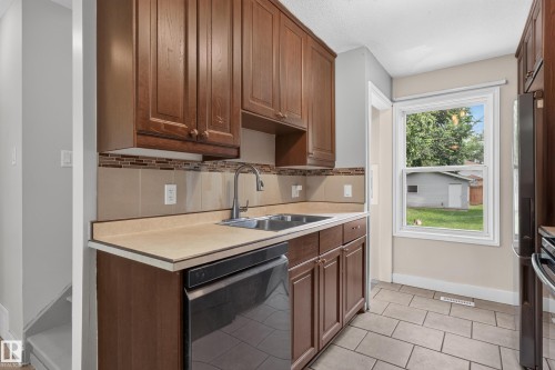 Kitchen featuring wood-finish cabinetry, tile backsplash, stainless steel sink, a dishwasher, and tile flooring - 11549 88 Street Nw, Edmonton, AB 