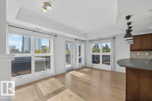 Recessed ceiling with crown molding, natural wood-finish flooring, multiple windows, and a glass-paneled door - #306 10232 115 St Nw, Edmonton, AB 