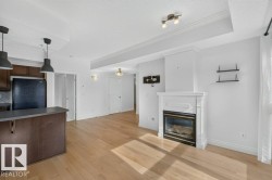 Wood-finish flooring, built-in fireplace with white mantel, tray ceiling, recessed lighting, and kitchen island with pendant lighting - 
