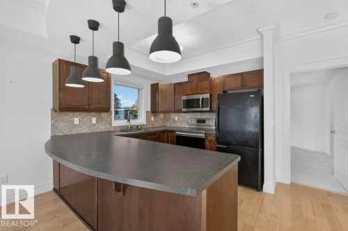 Kitchen featuring wood-finish flooring, dark wood cabinetry, stainless steel appliances, and pendant lighting - #306 10232 115 St Nw, Edmonton, AB 