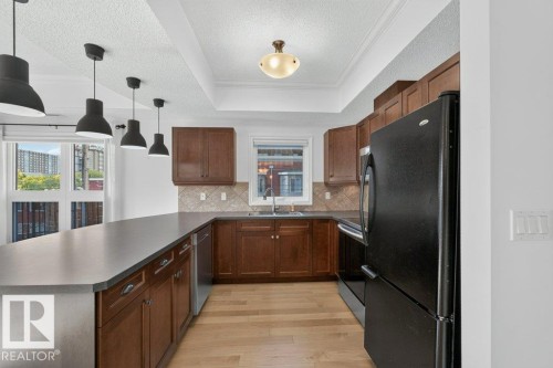 Kitchen featuring a U-shaped countertop, wood-finish cabinetry, a tile backsplash, and wood-finish flooring - #306 10232 115 St Nw, Edmonton, AB 