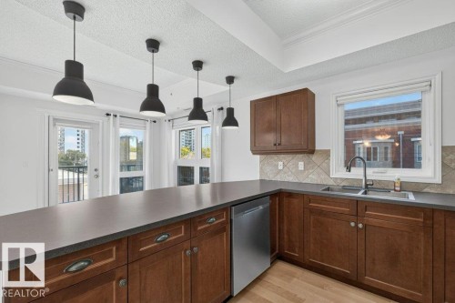 Kitchen featuring wood cabinetry, stainless steel dishwasher, dual basin sink with a gooseneck faucet, light wood-finish flooring, and pendant lighting - #306 10232 115 St Nw, Edmonton, AB 