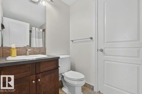 Wood-finish vanity with a rectangular basin sink, single-handle faucet, and tiled backsplash - #306 10232 115 St Nw, Edmonton, AB 