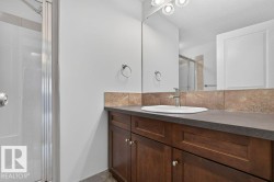 Bathroom featuring a spacious vanity with a built-in sink, wood-finish cabinetry, a broad mirror, and an adjacent shower with a glass enclosure - 