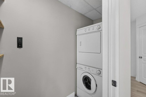 Stackable washer and dryer appliances, light gray wall finish, wood-finish flooring, white paneled door - #306 10232 115 St Nw, Edmonton, AB 