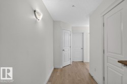 Hallway featuring wood-finish flooring, white panel doors, and a decorative wall sconce - 