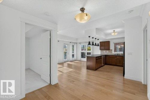 Hardwood flooring, kitchen island with pendant lighting, dark wood cabinetry, white trim, and a white interior door - #306 10232 115 St Nw, Edmonton, AB 