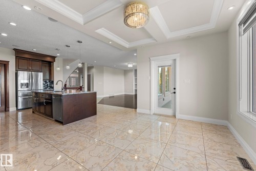Gleaming large format tile flooring, a kitchen island with built-in sink, stainless steel appliances, a coffered ceiling with a decorative chandelier, and a glass-paned door - 229 Albany Drive Nw, Edmonton, AB 