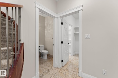 Carpeted staircase with wrought iron balusters, tiled flooring, white interior doors, and a built-in closet with shelving - 229 Albany Drive Nw, Edmonton, AB 