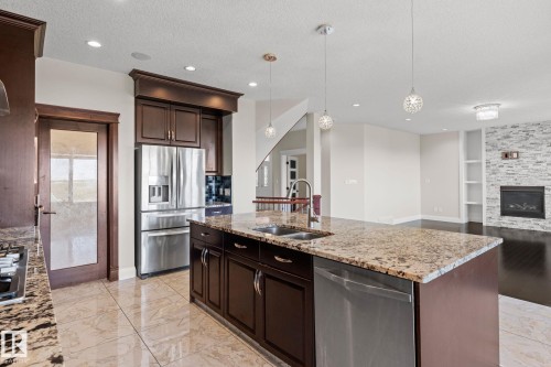 Kitchen featuring an oversized island with a dual-basin sink, stainless steel appliances, dark wood-finish cabinetry, and patterned floor tiling - 229 Albany Drive Nw, Edmonton, AB 