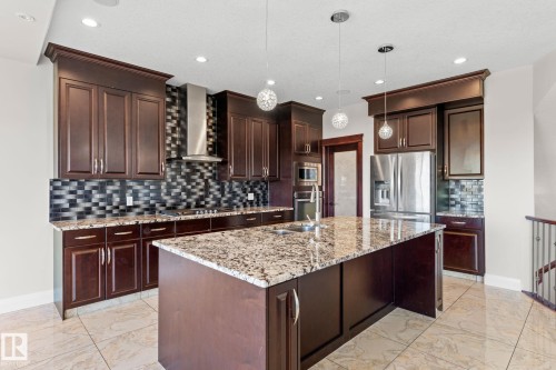 Kitchen featuring dark wood-finish cabinetry, stainless steel appliances, a spacious island with a light-toned countertop, and recessed lighting - 229 Albany Drive Nw, Edmonton, AB 