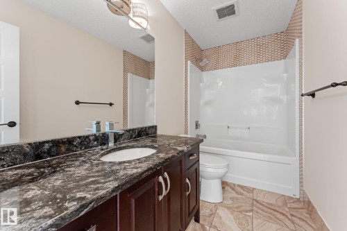 Vanity with a stone countertop, an undermount sink, and dark wood-finish cabinetry - 229 Albany Drive Nw, Edmonton, AB 