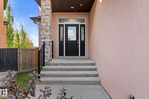 Stone facade detailing, a solid black entry door with decorative glass, and a black wrought iron railing enhance the approach to the property - 229 Albany Drive Nw, Edmonton, AB 