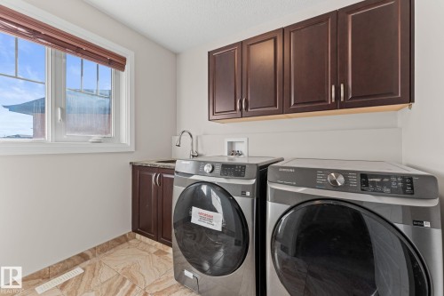 Laundry area featuring a window with blinds, wood-finish cabinetry, a sink with a chrome faucet, and tiled flooring - 229 Albany Drive Nw, Edmonton, AB 