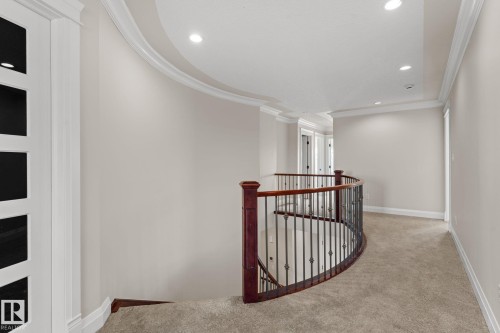 Curved staircase with wrought iron balusters and wood handrail, recessed lighting, crown molding, and neutral carpeting - 229 Albany Drive Nw, Edmonton, AB 