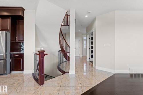 Curved staircase with wood railing and metal spindles, stainless steel refrigerator, dark wood-finish cabinetry, tile flooring, and dark wood-finish flooring - 229 Albany Drive Nw, Edmonton, AB 