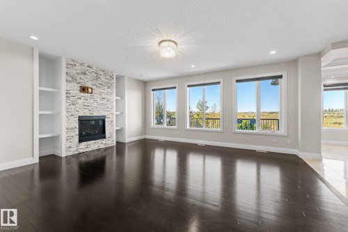Dark wood-finish flooring, stone-clad fireplace with built-in shelving, triple windows, recessed lighting, and a decorative ceiling fixture - 229 Albany Drive Nw, Edmonton, AB 