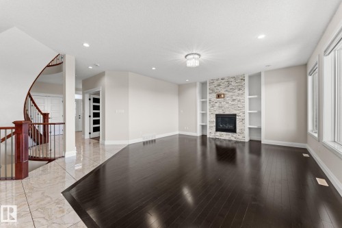 Dark wood-finish flooring, a stone-clad fireplace with built-in shelving, a modern chandelier, and a curved staircase with a wood handrail - 229 Albany Drive Nw, Edmonton, AB 