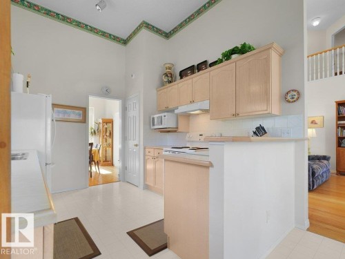 Kitchen featuring light wood-finish cabinetry, white tile flooring, white appliances, a white tile backsplash, and an architectural half wall - 156 Phillips Row Nw, Edmonton, AB 