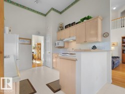 Kitchen featuring light wood-finish cabinetry, white tile flooring, white appliances, a white tile backsplash, and an architectural half wall - 