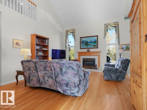 Vaulted ceiling with a white painted railing, wood-finish flooring, a fireplace with a wood mantle, and tall windows - 156 Phillips Row Nw, Edmonton, AB 
