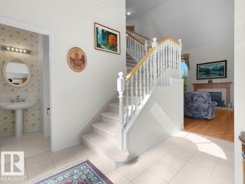 Tiled entry flooring, carpeted staircase with white balusters and wood-finish handrail, and a fireplace with wood-finish mantel - 156 Phillips Row Nw, Edmonton, AB 