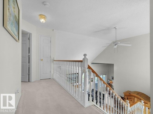 Upper hallawy, Carpeted hallway with white paneled doors, spindle railing, and a ceiling-mounted fan - 156 Phillips Row Nw, Edmonton, AB 