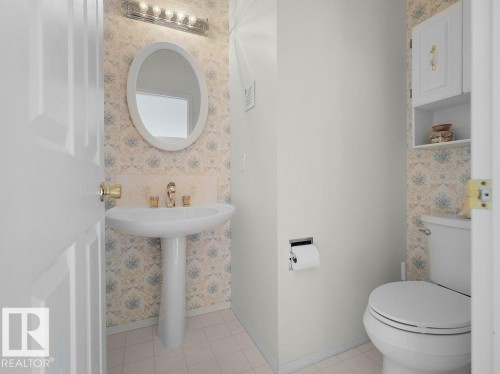 Main floor 2 pce. Pedestal sink with brass-finish faucet, overhead vanity lighting, and wall-mounted cabinetry - 156 Phillips Row Nw, Edmonton, AB 